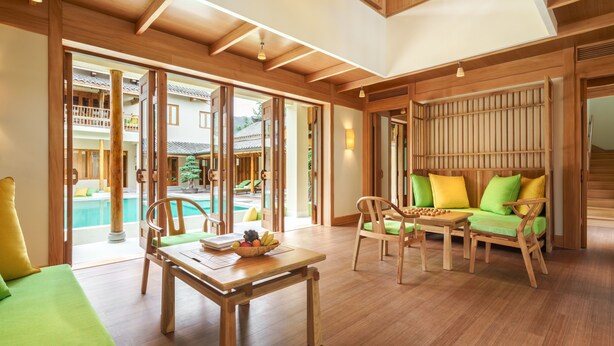 Una habitación amplia con suelo de madera, una mesa de comedor con sillas, un sofá y un balcón con vista a la piscina.