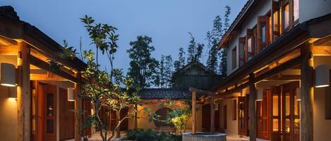 A courtyard with wooden pillars, a central seating area, and a traditional building with a tiled roof.