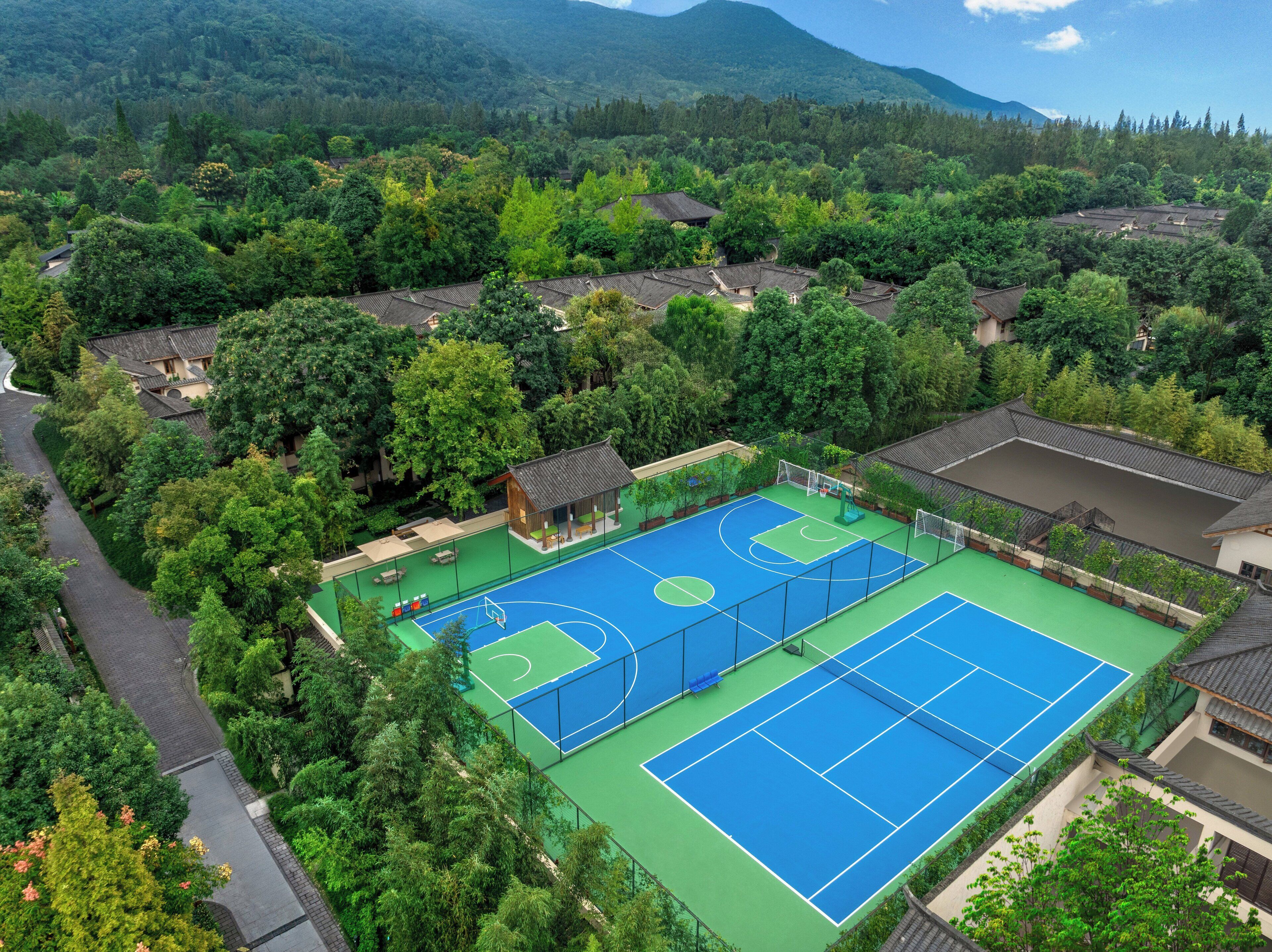 A tennis court surrounded by lush greenery and traditional architecture.