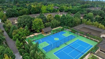 A tennis court surrounded by lush greenery and traditional architecture.