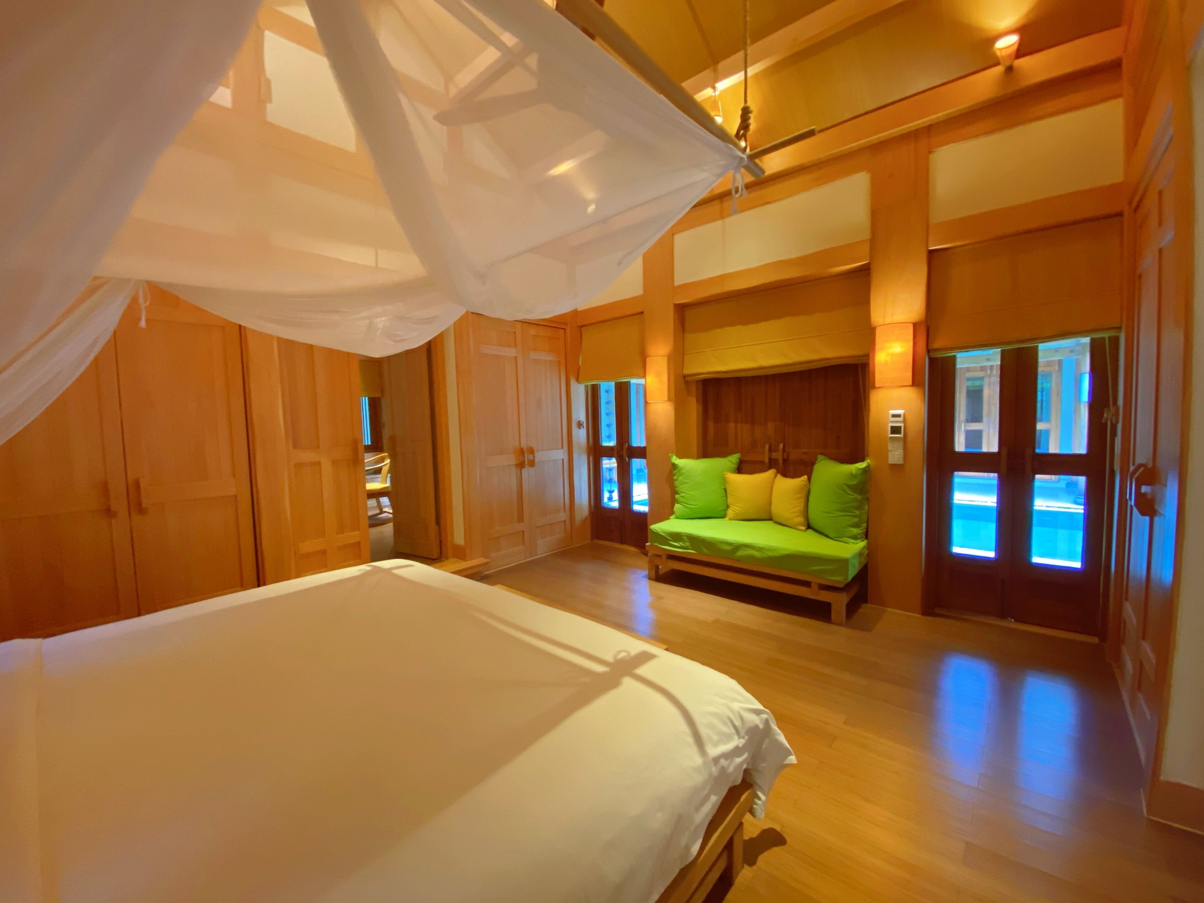 A spacious room with a large bed, a green sofa, wooden walls, and a ceiling fan.