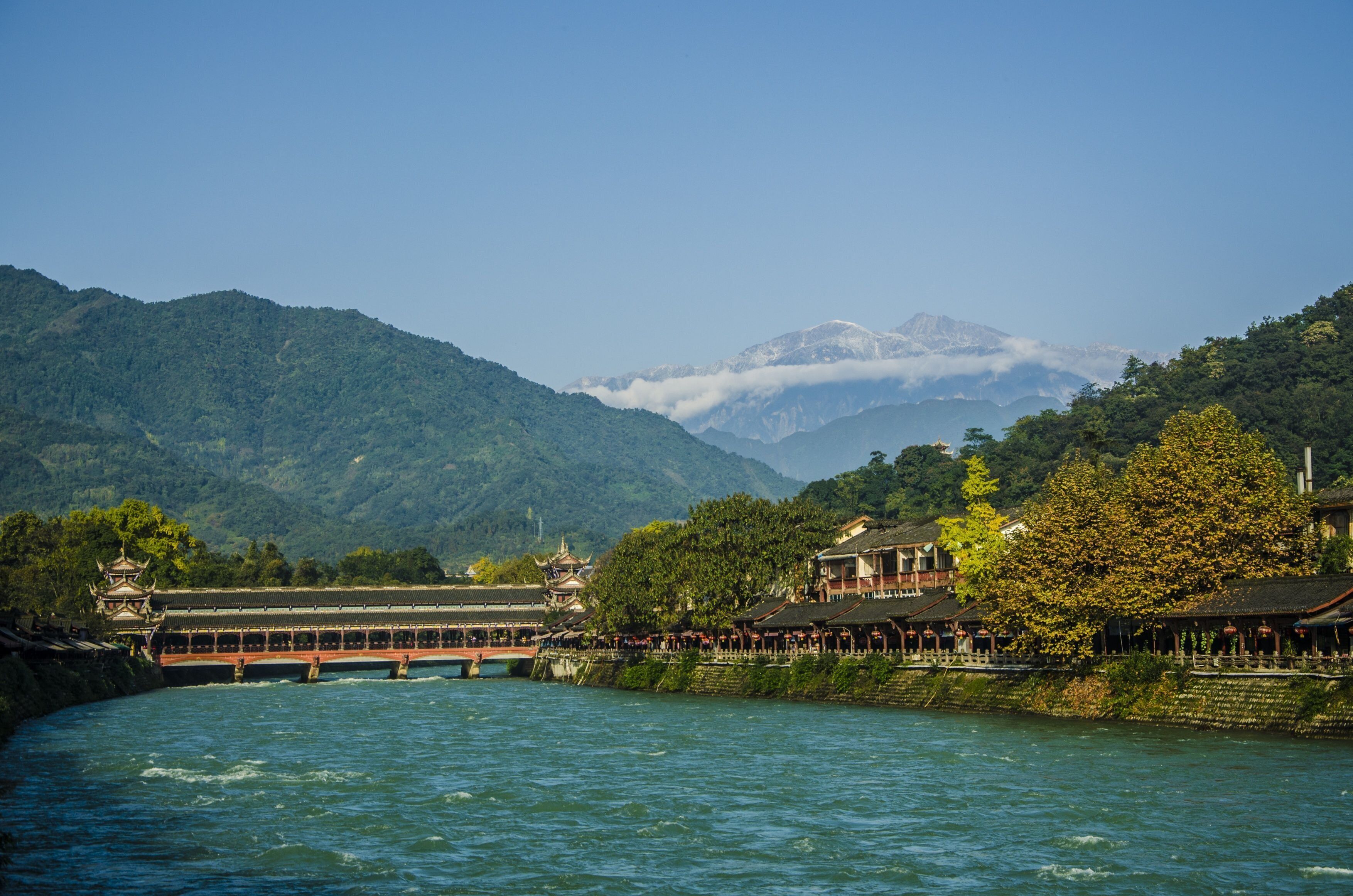 A riverside view with a traditional building and a bridge.
