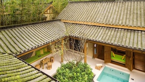 Un edificio de estilo tradicional con tejado de tejas, piscina y un exuberante jardín verde.