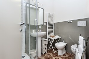 Un baño moderno con cabina de ducha de vidrio, lavamanos pedestal, bidé y toallero.