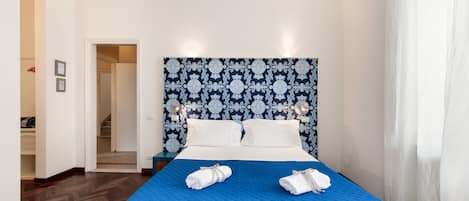 Habitación de hotel con una cama grande, un cabecero estampado y vistas a un pasillo.