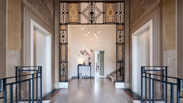 Una imponente entrada con piso de mármol, barandillas de metal negro y un techo decorativo.