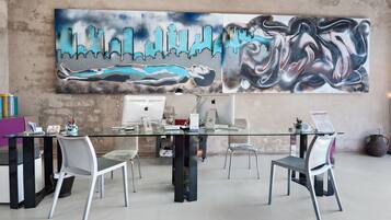 A modern office space with a glass table, metal chairs, and a large abstract painting on the wall.