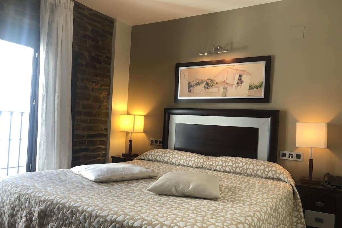 A hotel room with a large bed, two bedside lamps, a framed picture on the wall, and a stone accent wall.