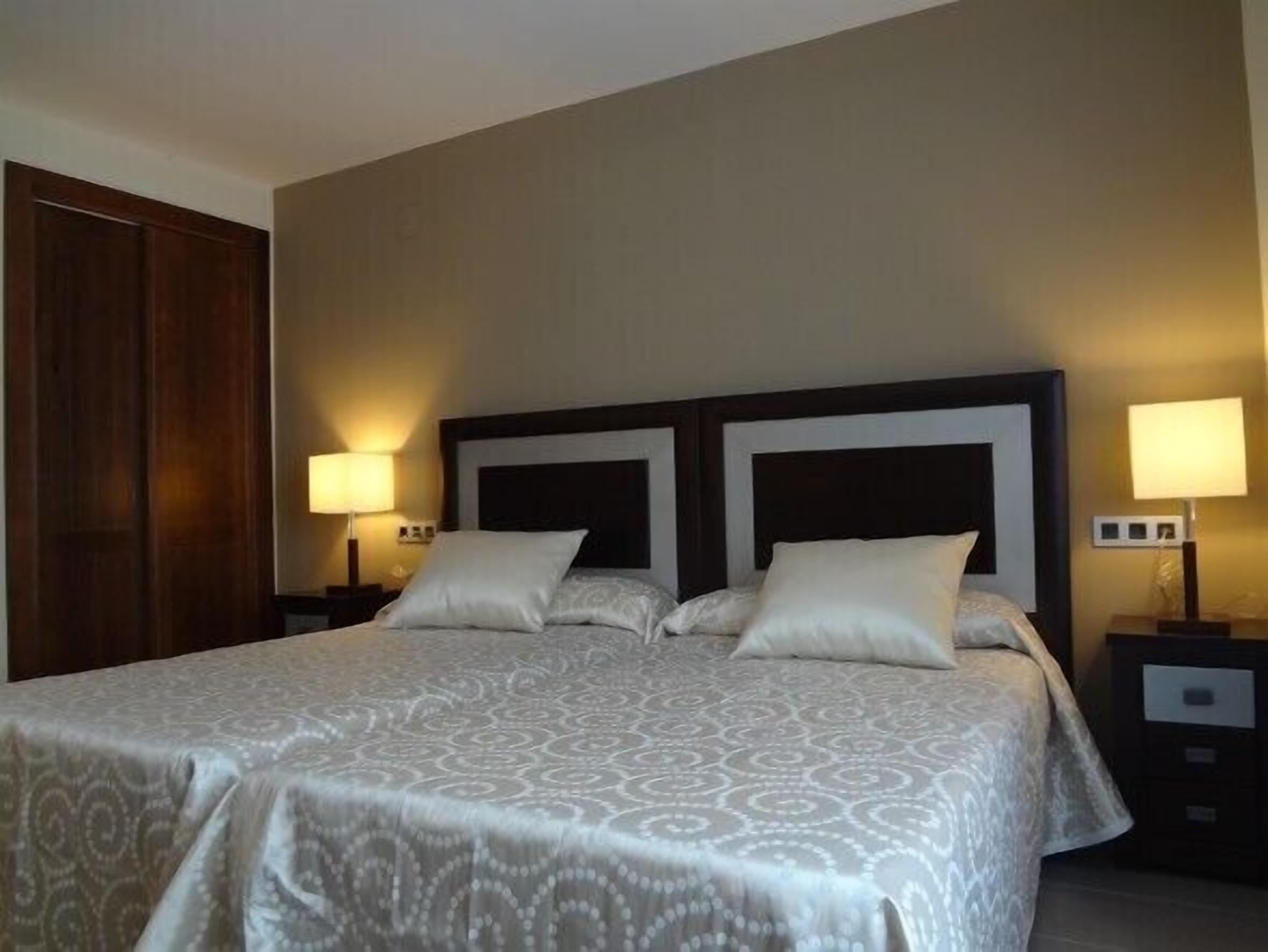 Una habitación de hotel con una cama grande, dos mesitas de noche y un armario de madera.