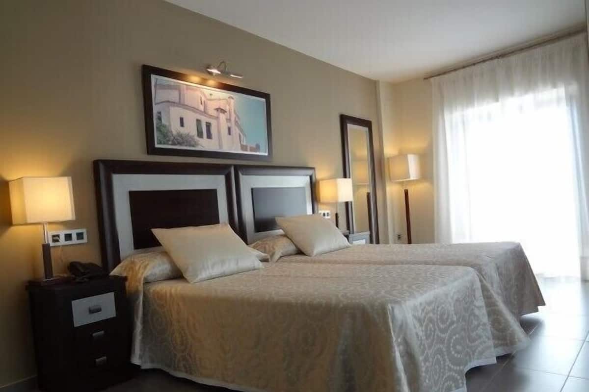 A hotel room with two beds, a nightstand, a lamp, and a painting on the wall.