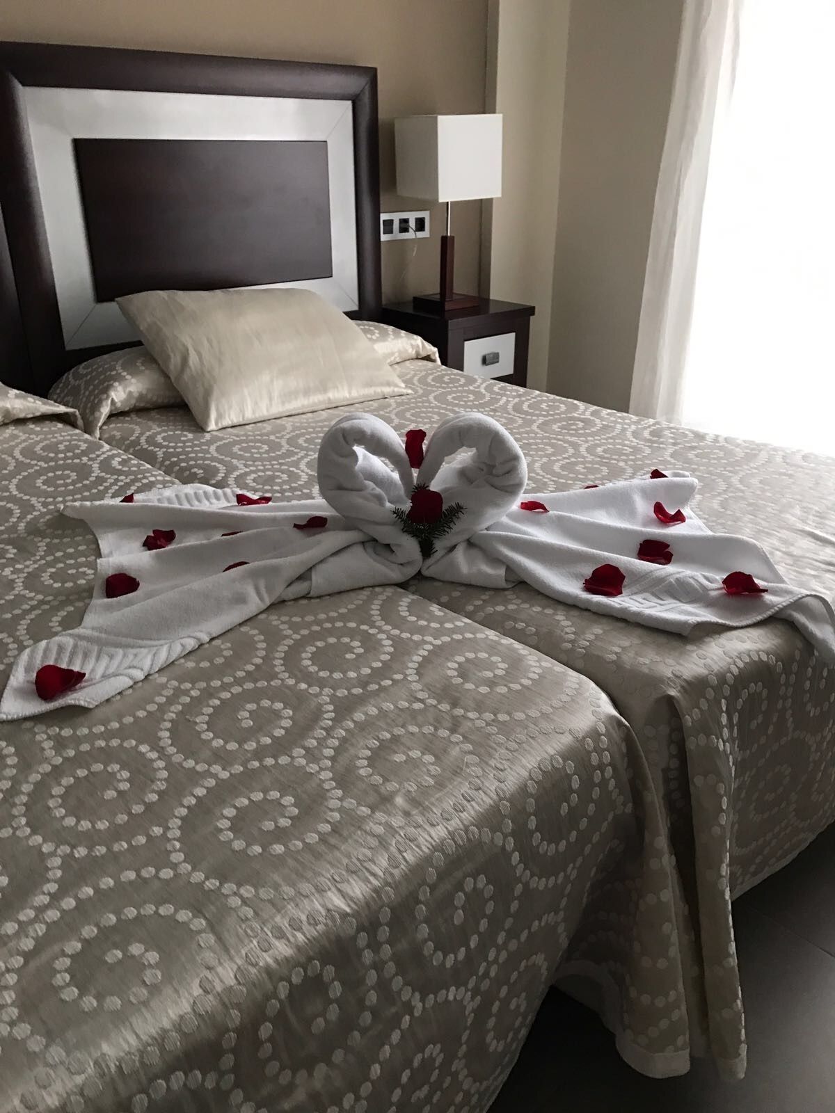 A neatly made bed with a towel arranged in a heart shape, adorned with rose petals.