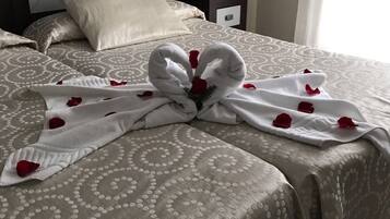 A neatly made bed with a towel arranged in a heart shape, adorned with rose petals.