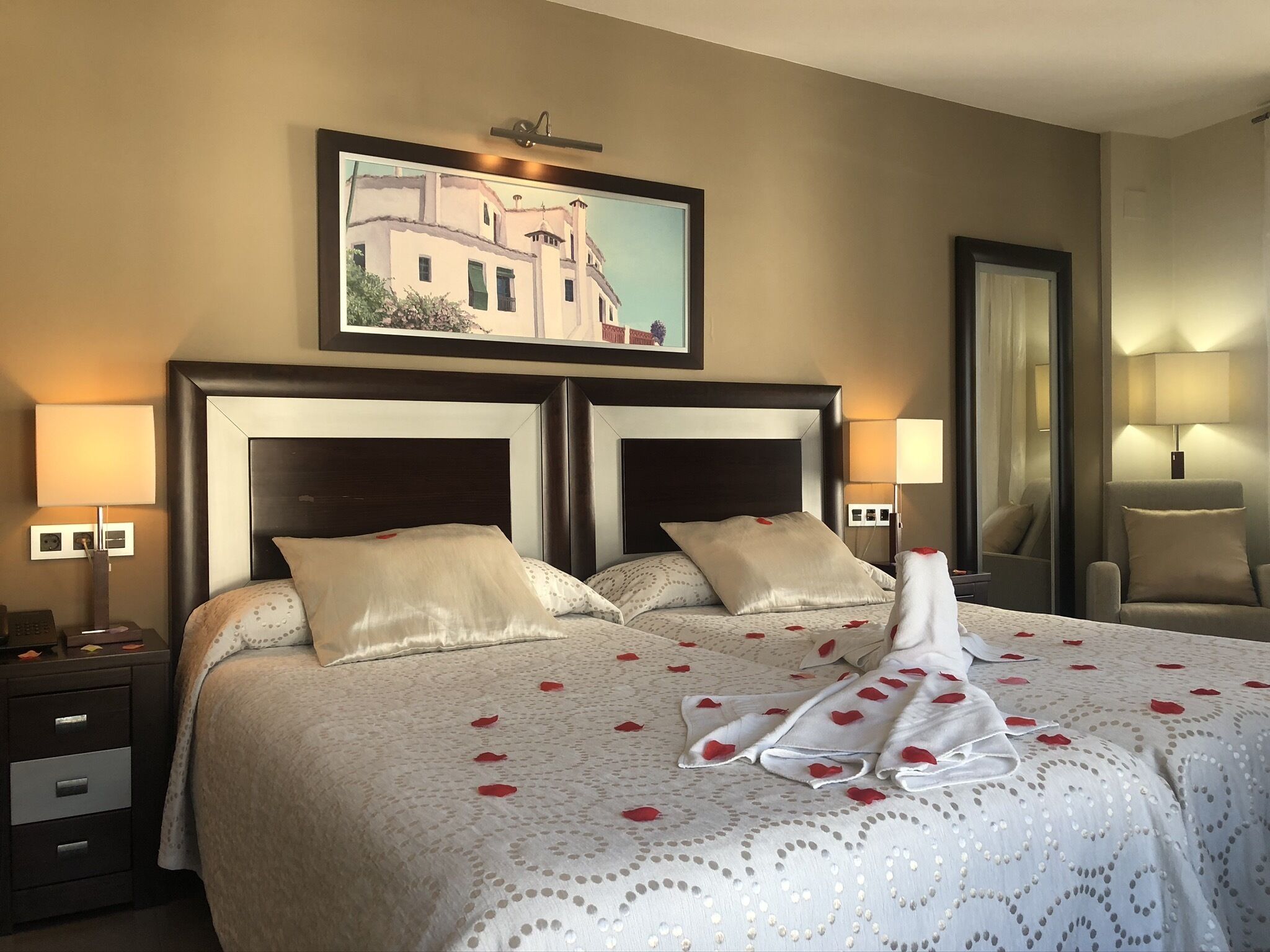 Una habitación de hotel con una cama grande, dos mesitas de noche, un tocador, un espejo y un cuadro en la pared.