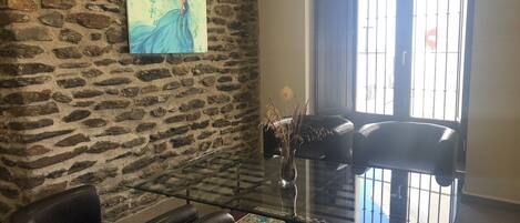 A lobby with a stone wall, a glass coffee table, leather chairs, a vase with dried plants, and a painting.