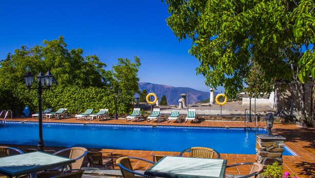 Zona junto a la piscina con sillas de descanso, una mesa y vistas a las montañas.
