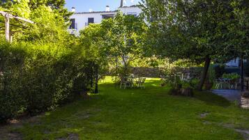 Un jardín con una mesa y sillas, un edificio al fondo y un cielo despejado.