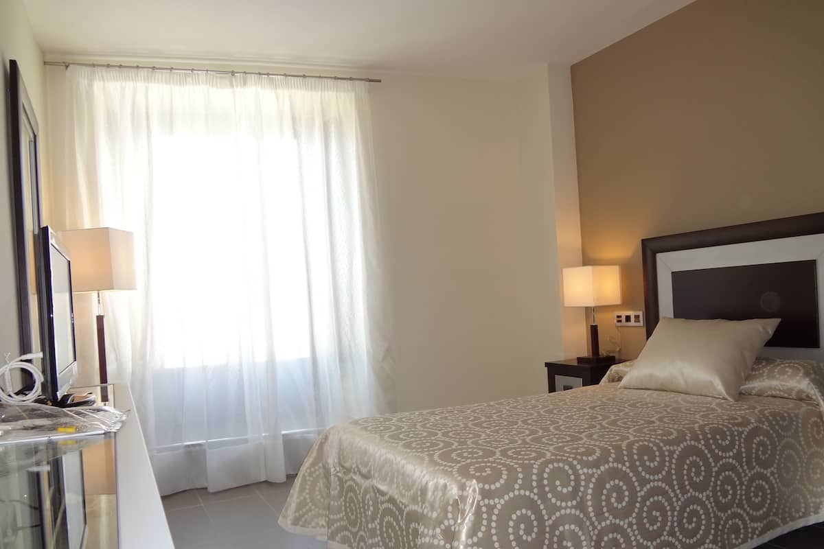 A hotel room with a bed, bedside lamps, a desk with a computer, and a window with curtains.