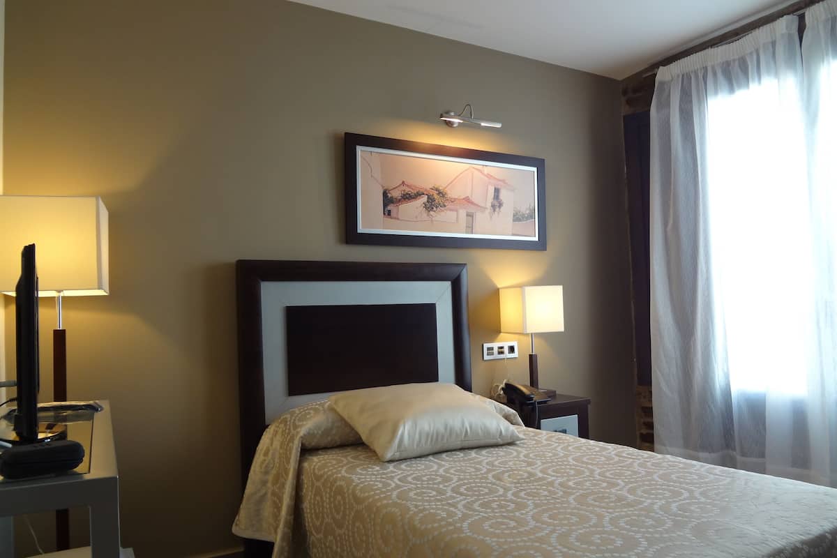 A hotel room with a bed, two bedside lamps, a framed picture on the wall, and a window with curtains.