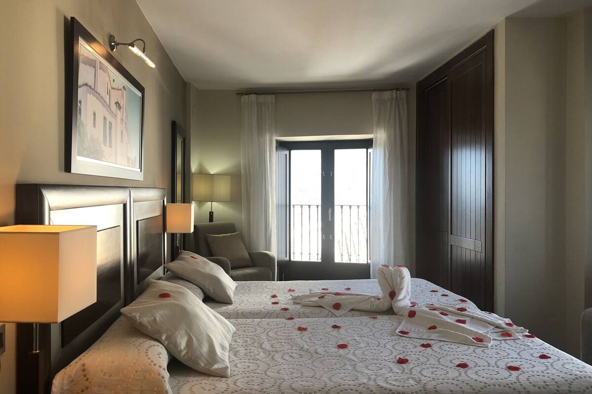 A hotel room with a large bed, a chair, a desk, a lamp, and a window with curtains.