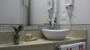 A bathroom with a white sink, a mirror, a towel rack with towels, and a hairdryer on the wall. - Hotel Merlott Lleras (Medellín)
