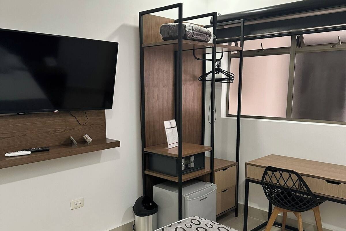 Habitación de hotel pequeña con literas, un escritorio con silla, televisor y una alfombra estampada.