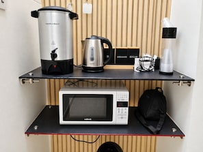 Un coin cuisine équipé d’un four à micro-ondes, d’une mijoteuse, d’une machine à café et d’une bouilloire, le tout posé sur un plan de travail noir.