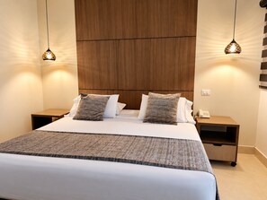 A hotel room with a large bed, two bedside tables, a wooden headboard, and pendant lighting. - Hotel Merlott Lleras (Medellín)