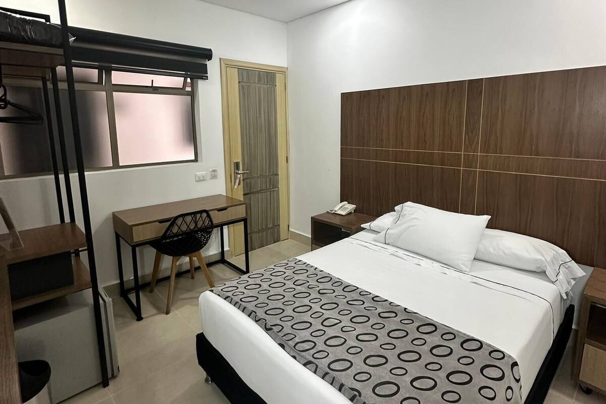 Una habitación de hotel moderna con literas, un escritorio, una silla, una mesita de noche con un teléfono y una colcha estampada.