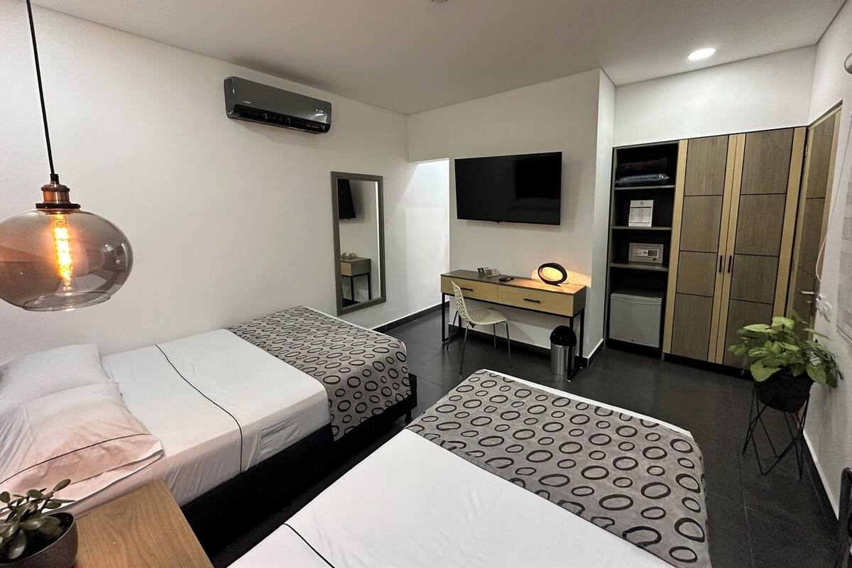 Una habitación de hotel moderna con dos camas, un escritorio, un televisor, un armario y una lámpara colgante.