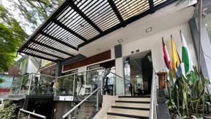 Entrada de un hotel con una escalera de cristal, un área cubierta con vigas de metal y varias banderas.