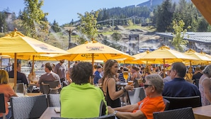 An outdoor seating area with yellow umbrellas, tables, and chairs. - Carleton Lodge (Whistler)