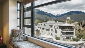 A room with a large window overlooking a mountainous landscape, featuring a seating area with a patterned cushion and a red chair. - Carleton Lodge (Whistler)