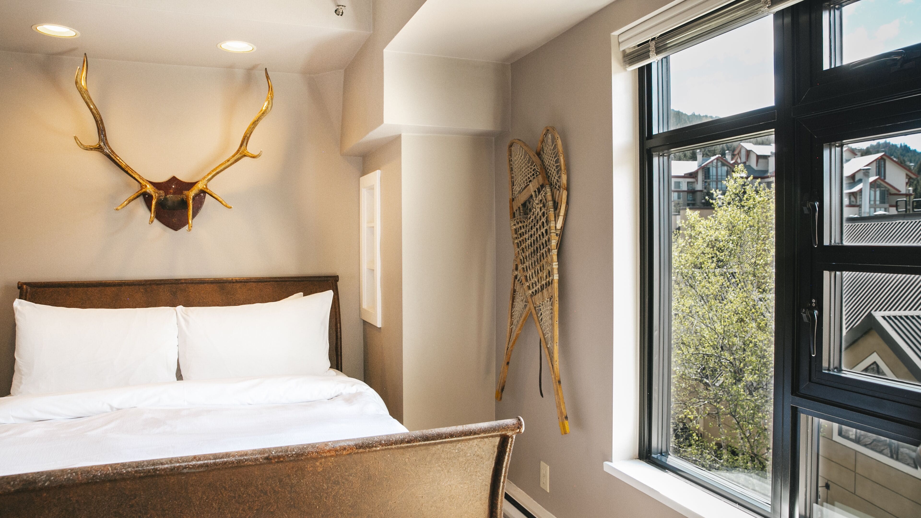 A bed with white linens, a wooden headboard, and a mounted antler on the wall.