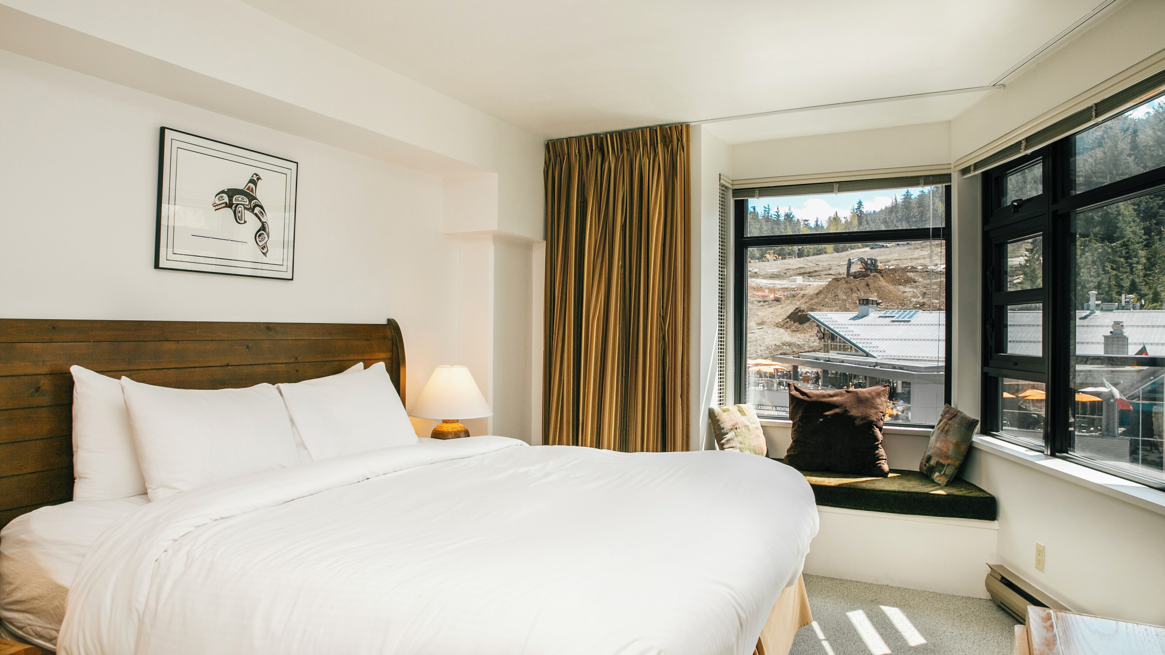 Una habitació d'hotel amb un llit, una finestra que mostra una vista de construcció, una fotografia encadrada a la paret i una cortina.