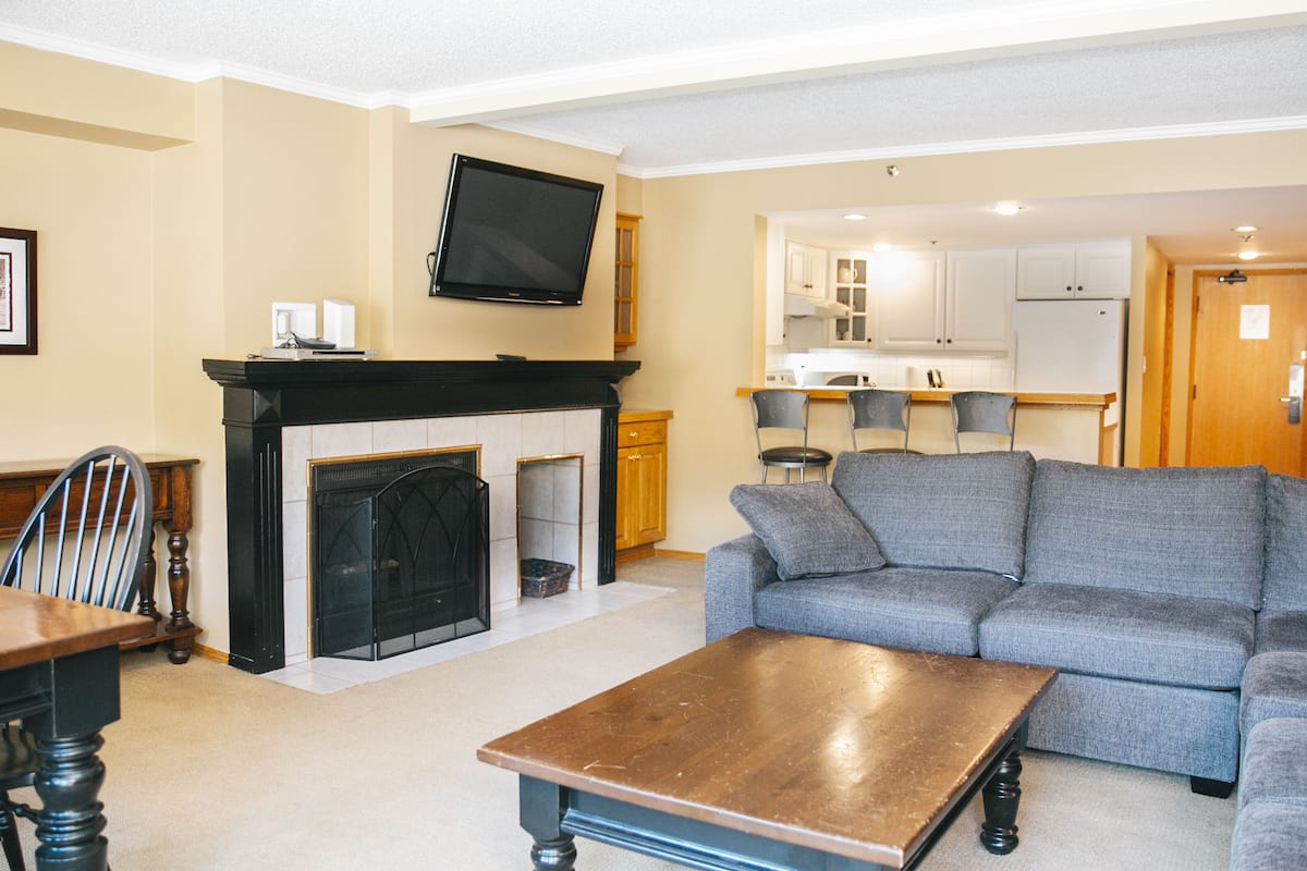 A living room with a fireplace, a sofa, a coffee table, and a TV mounted on the wall.