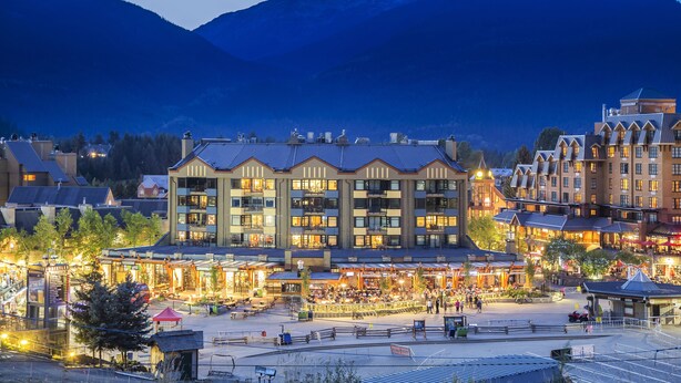 A hotel with multiple floors, a central courtyard, and a mountain backdrop. - Carleton Lodge (Whistler)