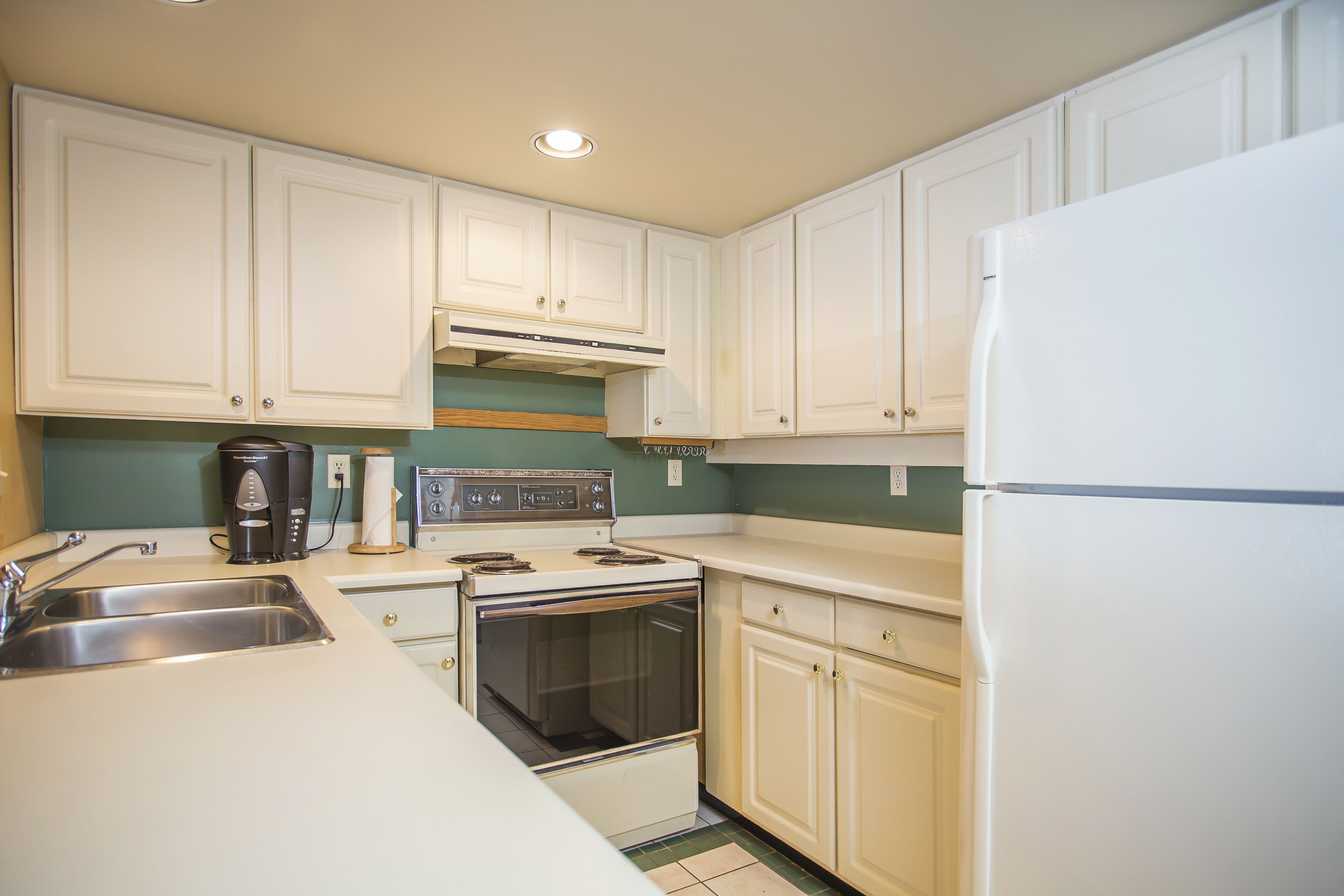 A kitchen with white cabinets, a stove, a sink, and a refrigerator.