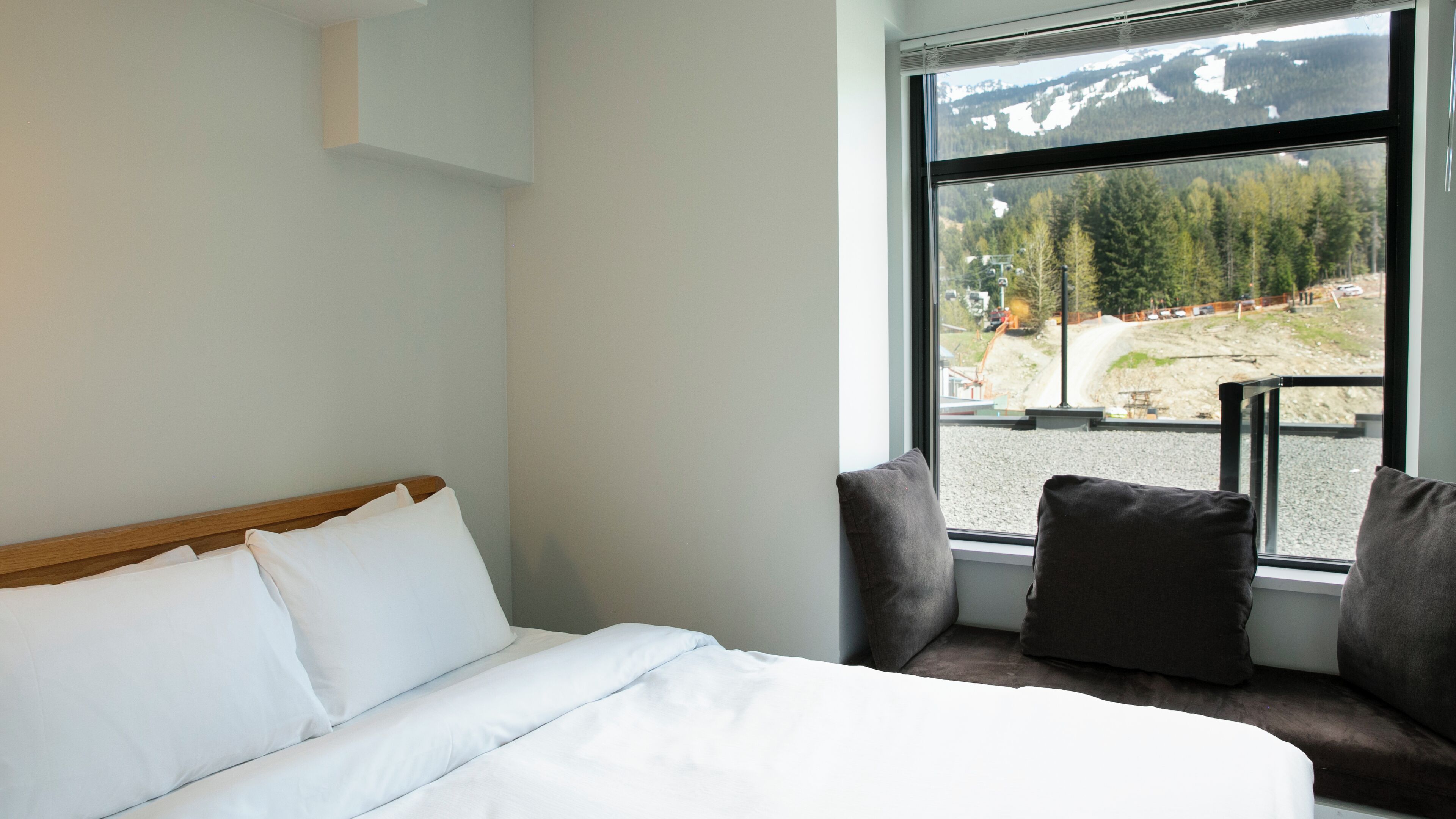 A bedroom with a large window, a bed with white linens, and a view of a construction site.