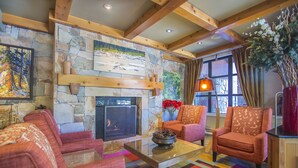 A cozy living room with a stone fireplace, wooden beams, and colorful carpet. - Carleton Lodge (Whistler)