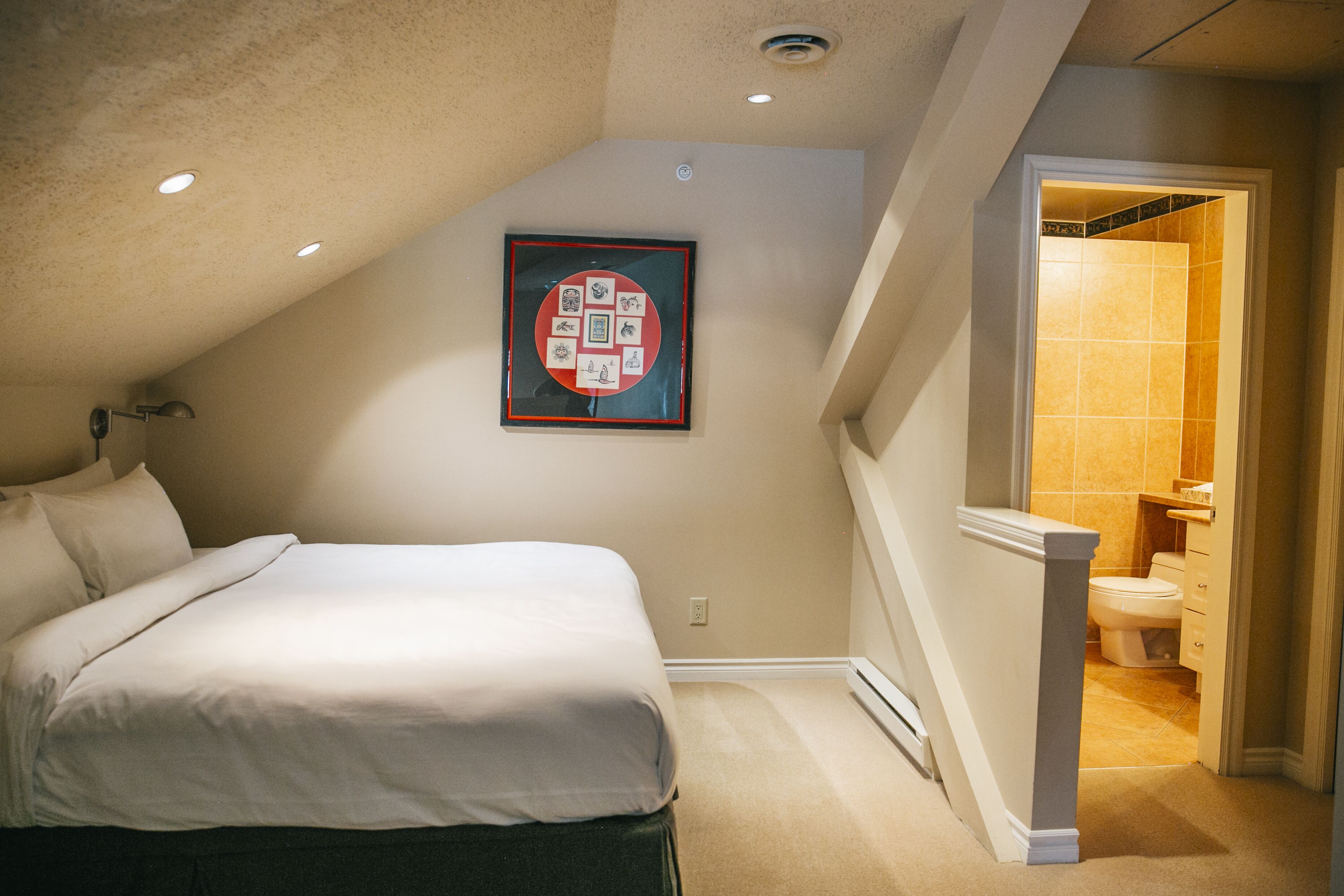 A bedroom with a bed, a framed artwork on the wall, and a bathroom visible through an open door.