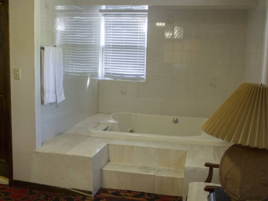 Un baño con bañera, una ventana con persianas, un perchero para toallas y una lámpara.