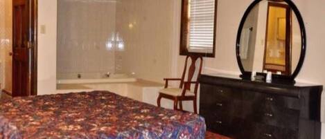 A bedroom with a bed, a chair, a dresser, a mirror, and a window with blinds.