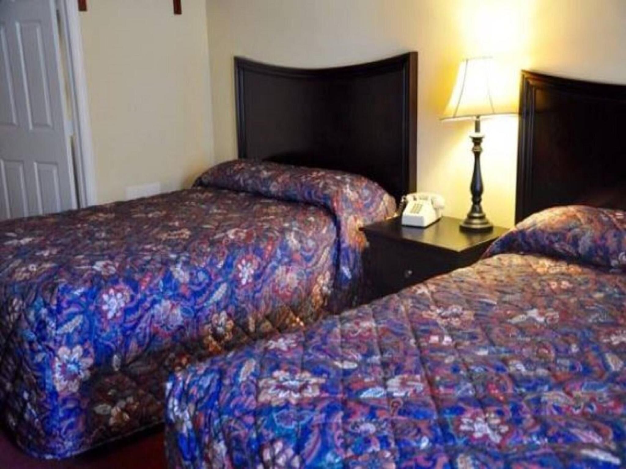 Una habitación de hotel con dos camas, cada una con colcha estampada de flores, una mesita de noche con lámpara y teléfono.