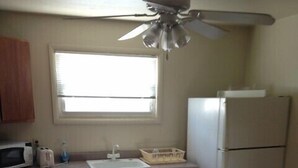 A kitchen with wooden cabinets, a white refrigerator, a microwave, a sink, and a ceiling fan. - Countryside Motel (Cold Spring)