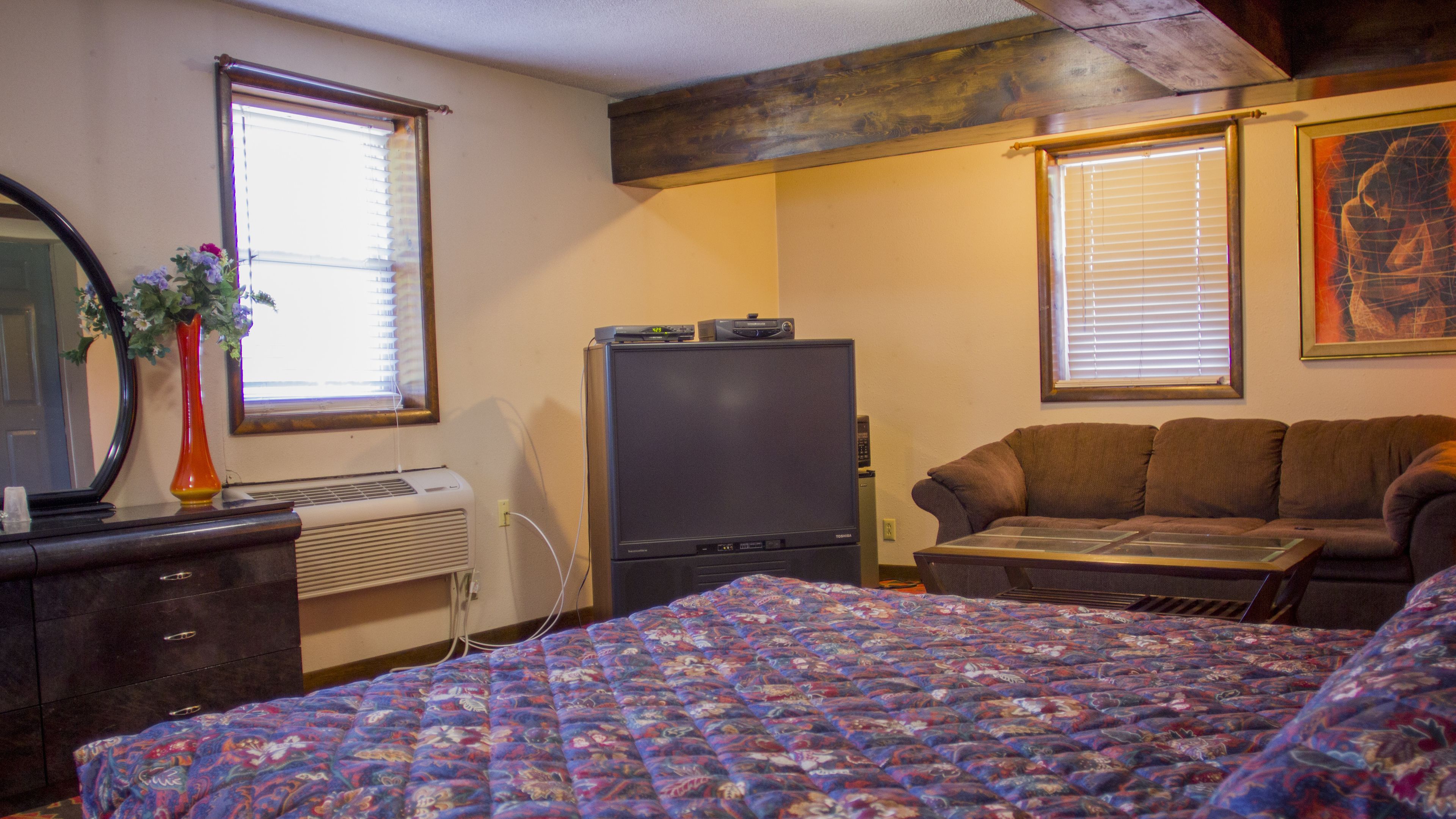 A bedroom with a bed, dresser, TV, and a couch.