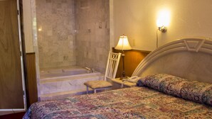 A hotel room with a large bed, a bathroom with a bathtub, and a shower. - Countryside Motel (Cold Spring)