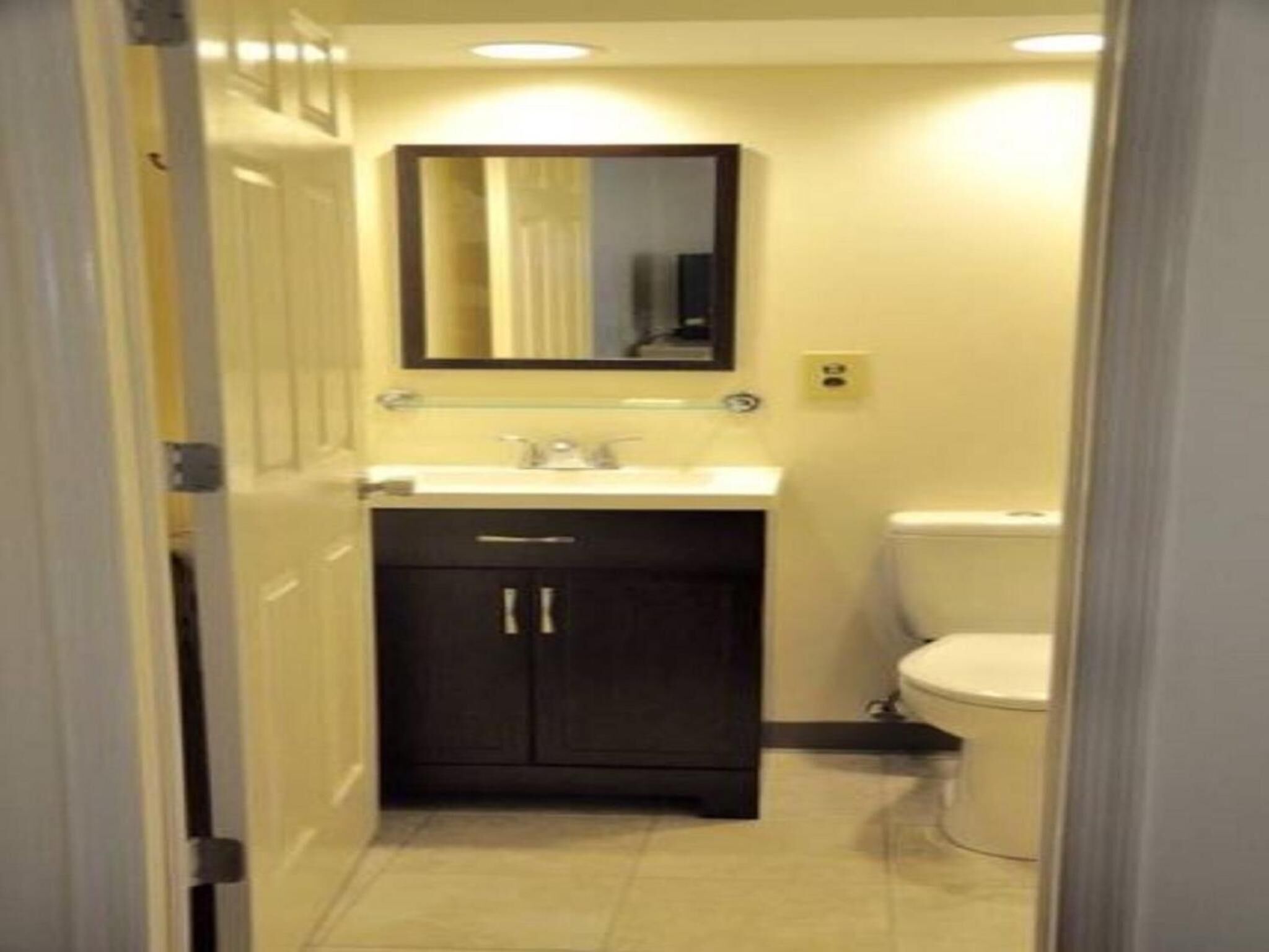 A narrow bathroom with a white sink, dark cabinets, and a toilet.