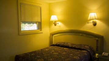 A hotel room with a bed, two wall-mounted lamps, a window with blinds, and a telephone on a bedside table.