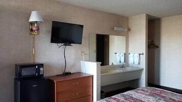 A hotel room with a flat-screen TV, a microwave, a dresser, a bed with a patterned bedspread, a sink, and a mirror.