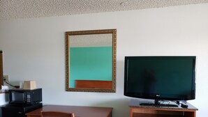 Habitación de hotel con un escritorio de madera, televisor sobre un soporte, una silla, microondas y un armario.